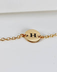 A gold chain bracelet featuring a circular disk engraved with the letter H.