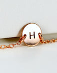 A close-up view of a rose gold circular charm engraved with the letter H on a delicate rose gold chain.