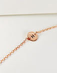 A delicate rose gold chain bracelet with a tiny round initial disk showing the letter H.