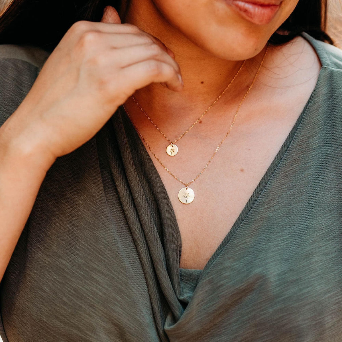 A person wearing two gold chain necklaces with small and large engraved round disc pendants.
