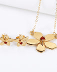 A set of gold jewelry consisting of two flower stud earrings and a matching flower pendant necklace with red gemstone centers.