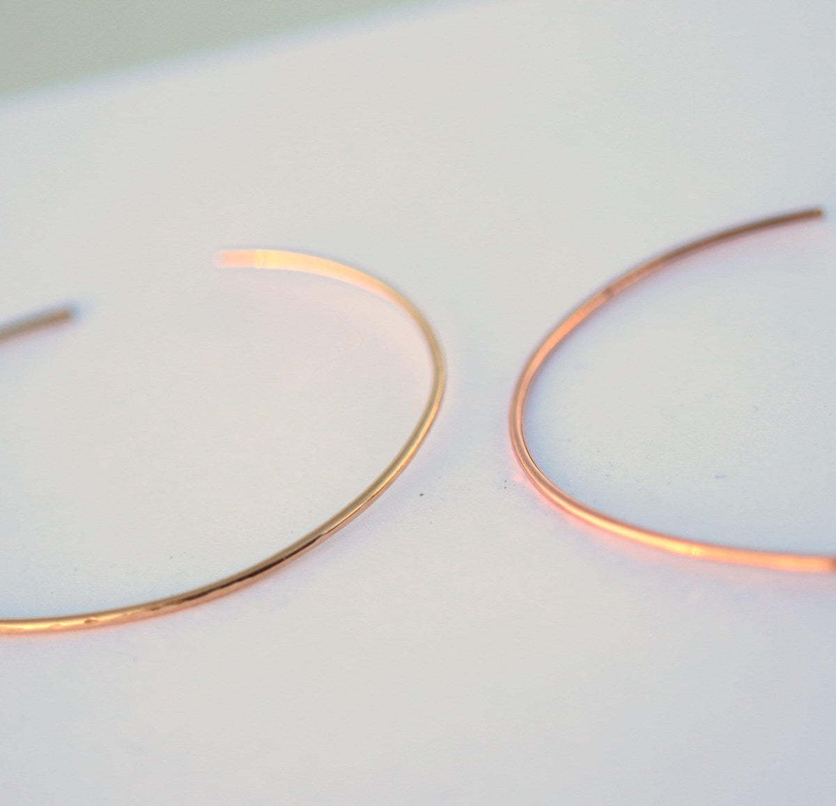 Two thin rose gold cuff bracelets are positioned side by side on a plain light background.