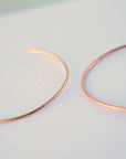 Two thin rose gold cuff bracelets are positioned side by side on a plain light background.