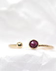Frontal view of the gold open ring with a textured band, featuring a round ruby and a ball terminal against a white crinkled background.