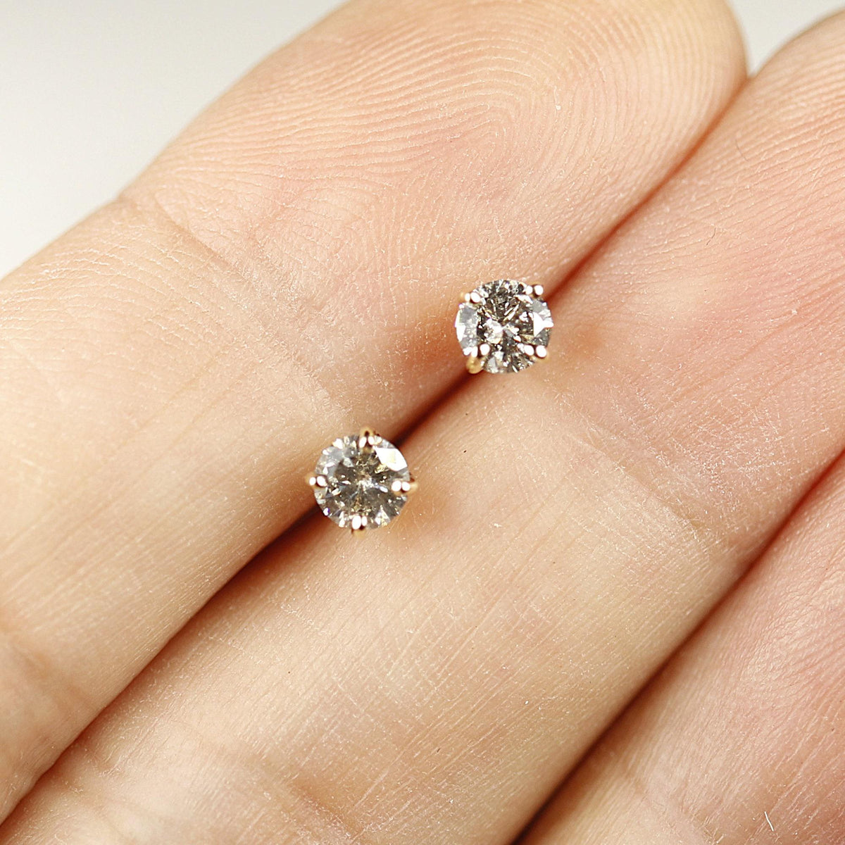 Two salt and pepper diamond stud earrings resting on a person&amp;