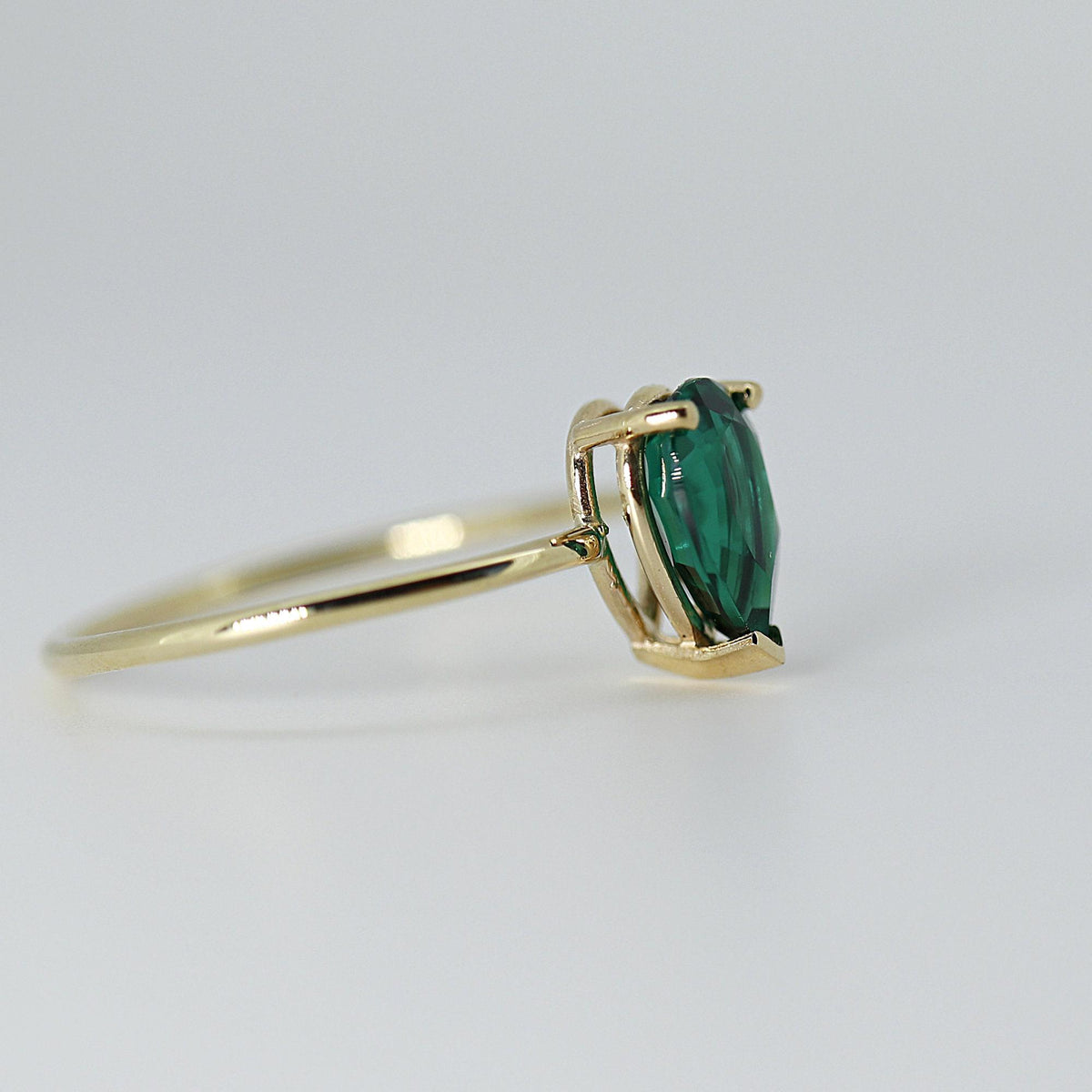 Profile view of the gold ring showing the gallery and setting of the pear-cut green stone.