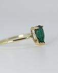 Profile view of the gold ring showing the gallery and setting of the pear-cut green stone.