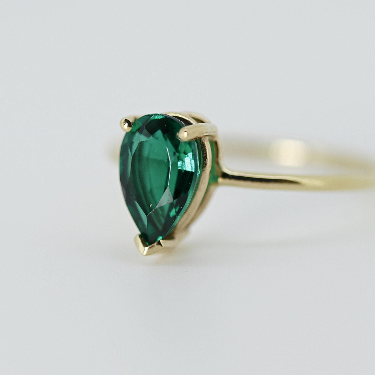 Three-quarter angle view of the pear-shaped green gemstone ring on a neutral white surface.