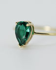 Three-quarter angle view of the pear-shaped green gemstone ring on a neutral white surface.