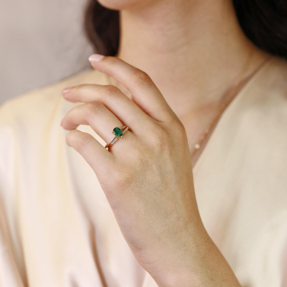 A person wears a small pear-cut green emerald ring with a delicate diamond band on their ring finger.