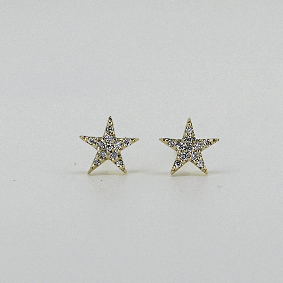 A pair of gold star-shaped stud earrings inset with small clear stones, presented on a light background.