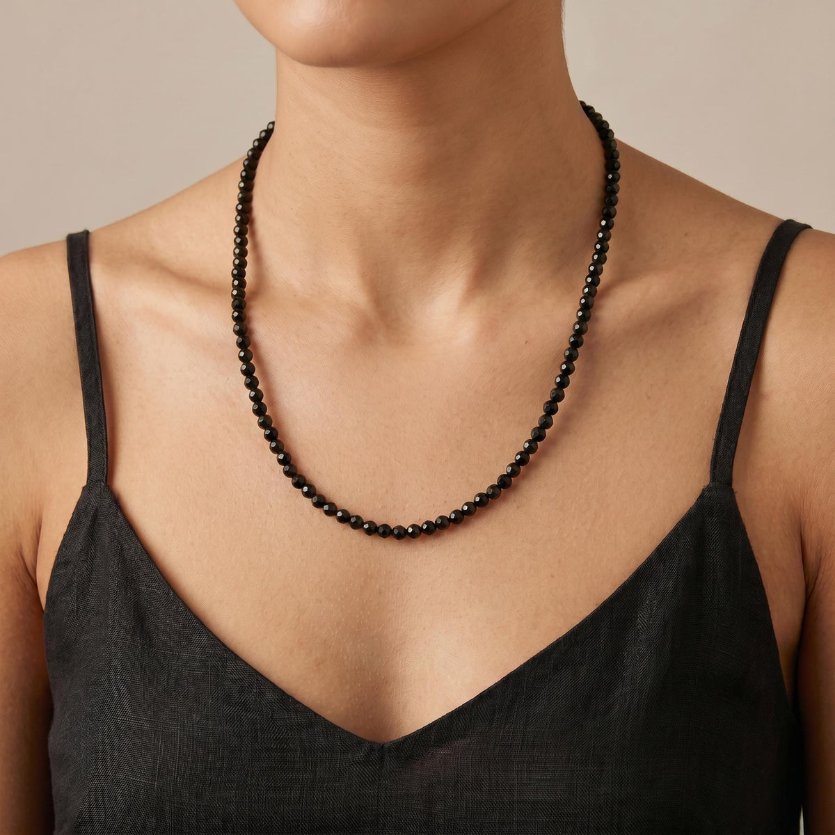 A person wearing a black faceted bead necklace and a black tank top.