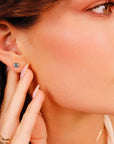 Close up of a person wearing a triangle-cut blue gemstone stud earring in their earlobe.