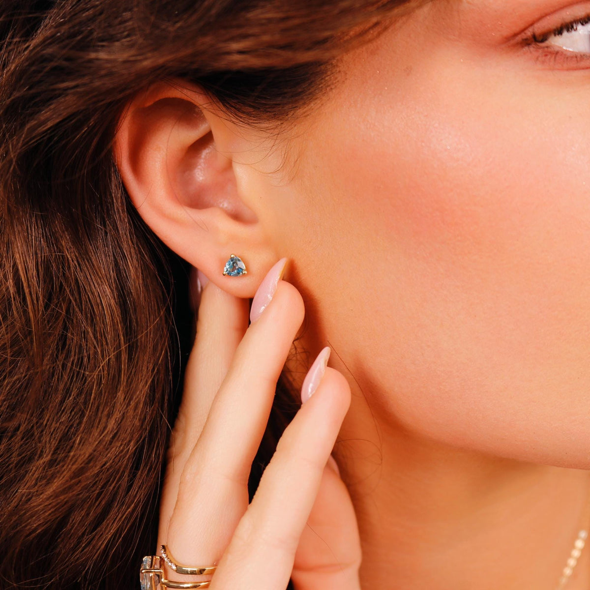Close-up portrait of a person wearing a single blue gemstone stud earring and rings on their fingers.