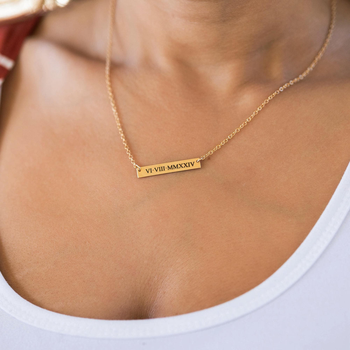 Close-up of a person wearing a gold bar necklace engraved with the roman numerals VI-VIII-MMXXIV.