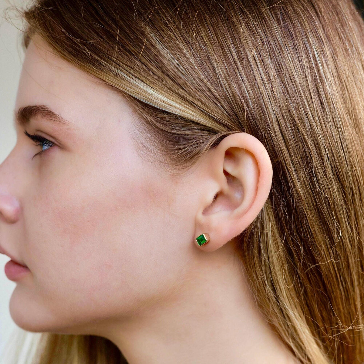 Profile shot of a woman with long hair wearing a small emerald stud earring.