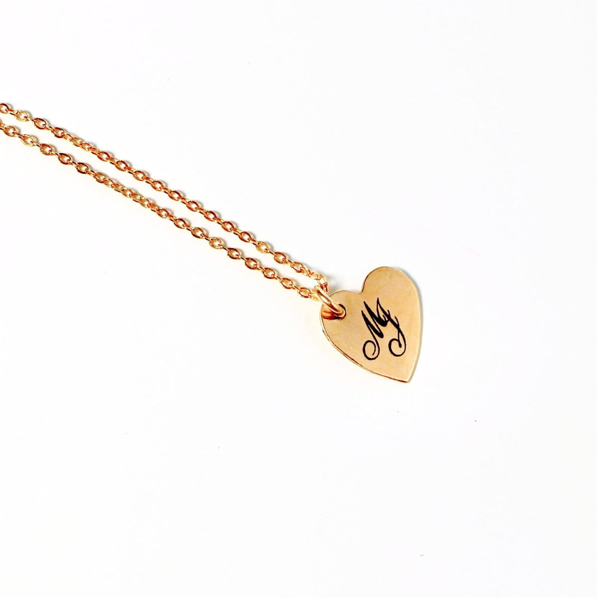 Close-up of a gold heart charm engraved with script letters on a white background.