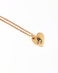 Close-up of a gold heart charm engraved with script letters on a white background.