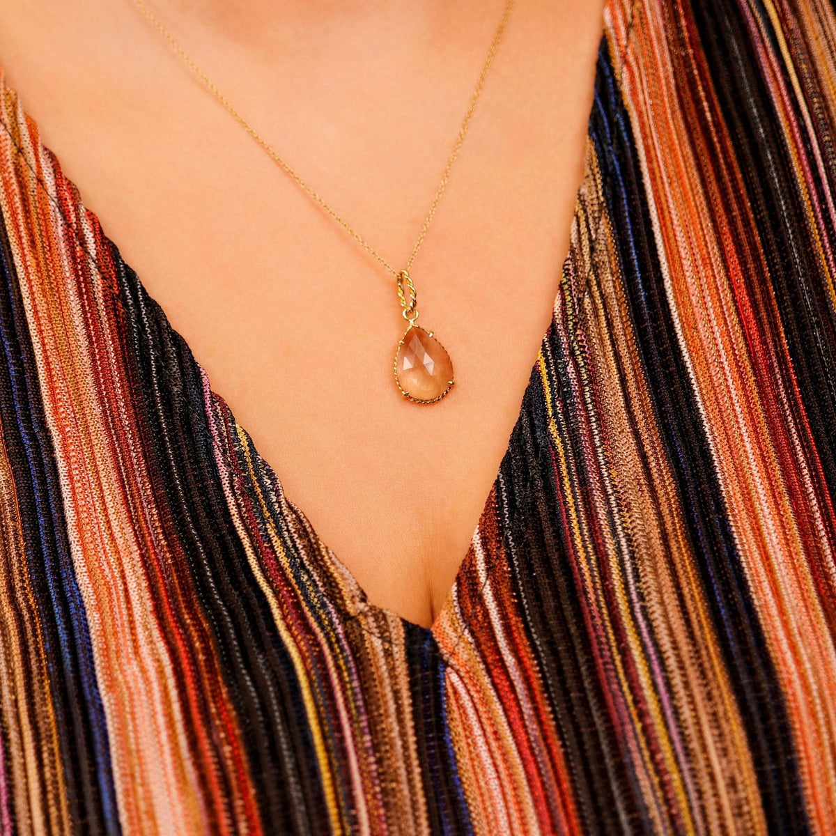 A faceted pear-shaped smokey quartz pendant hangs from a thin gold chain worn against a vertically striped shirt.
