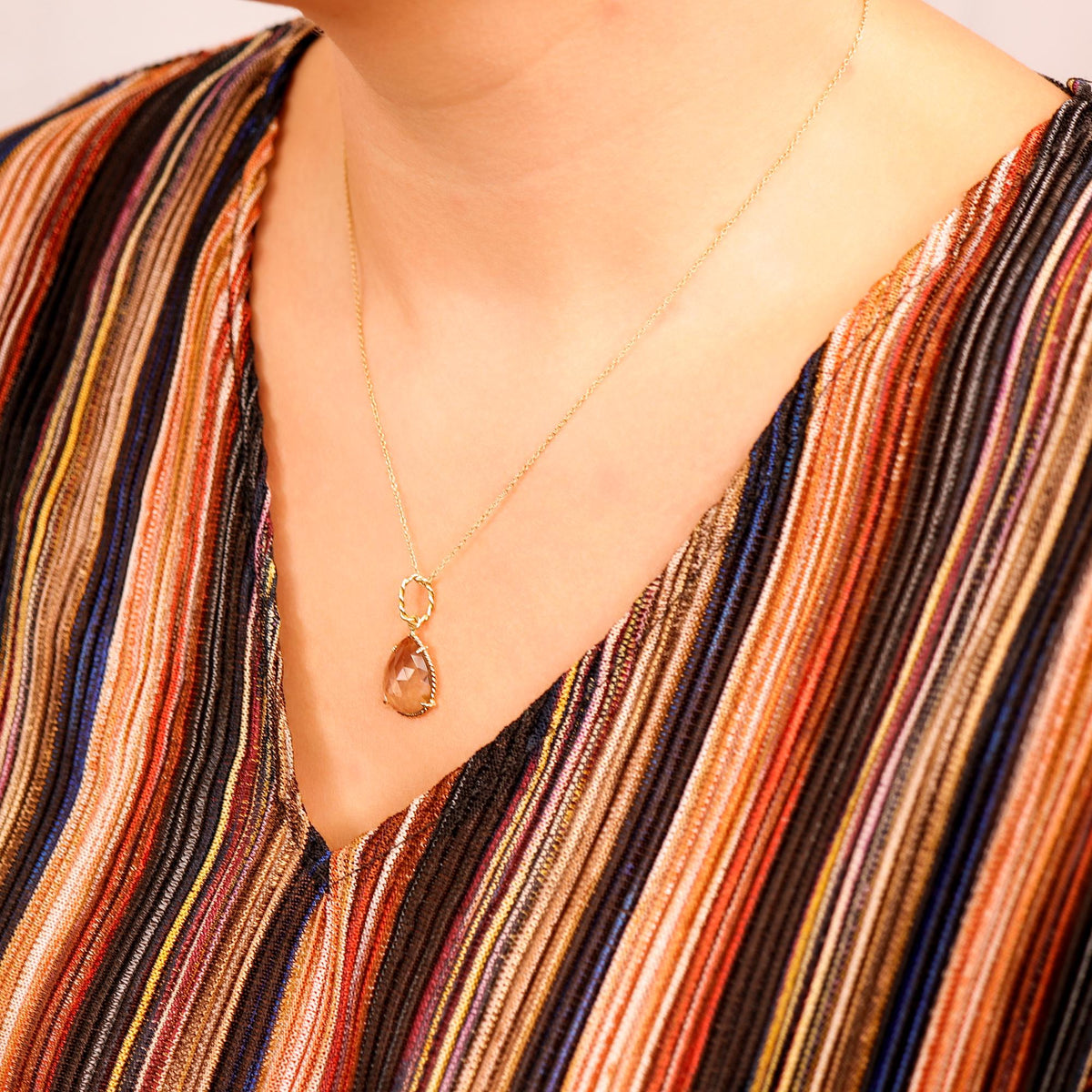 A pear-shaped pendant on a delicate chain rests below the collarbone of a person wearing a multi-colored striped top.