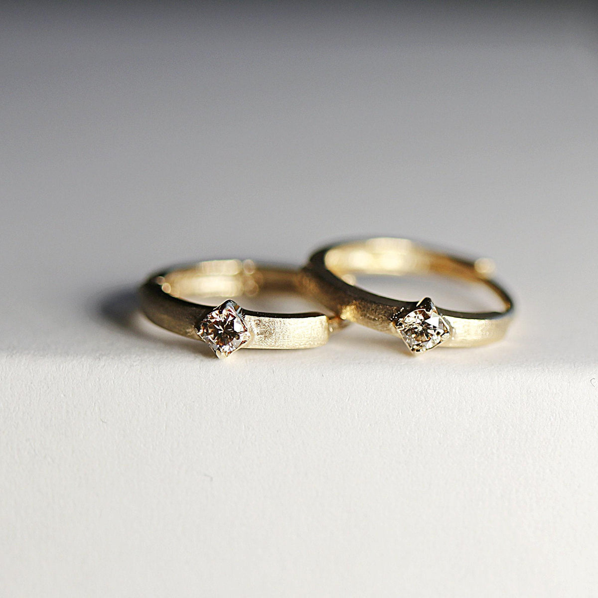 Two gold huggie hoop earrings with single diamonds rest closely together on a white background, viewed from a slightly angled perspective.