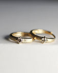 Two gold huggie hoop earrings with single diamonds rest closely together on a white background, viewed from a slightly angled perspective.