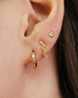 Close-up of a pierced ear wearing a gold diamond huggie hoop earring, a gold lightning bolt stud, and a round diamond stud.