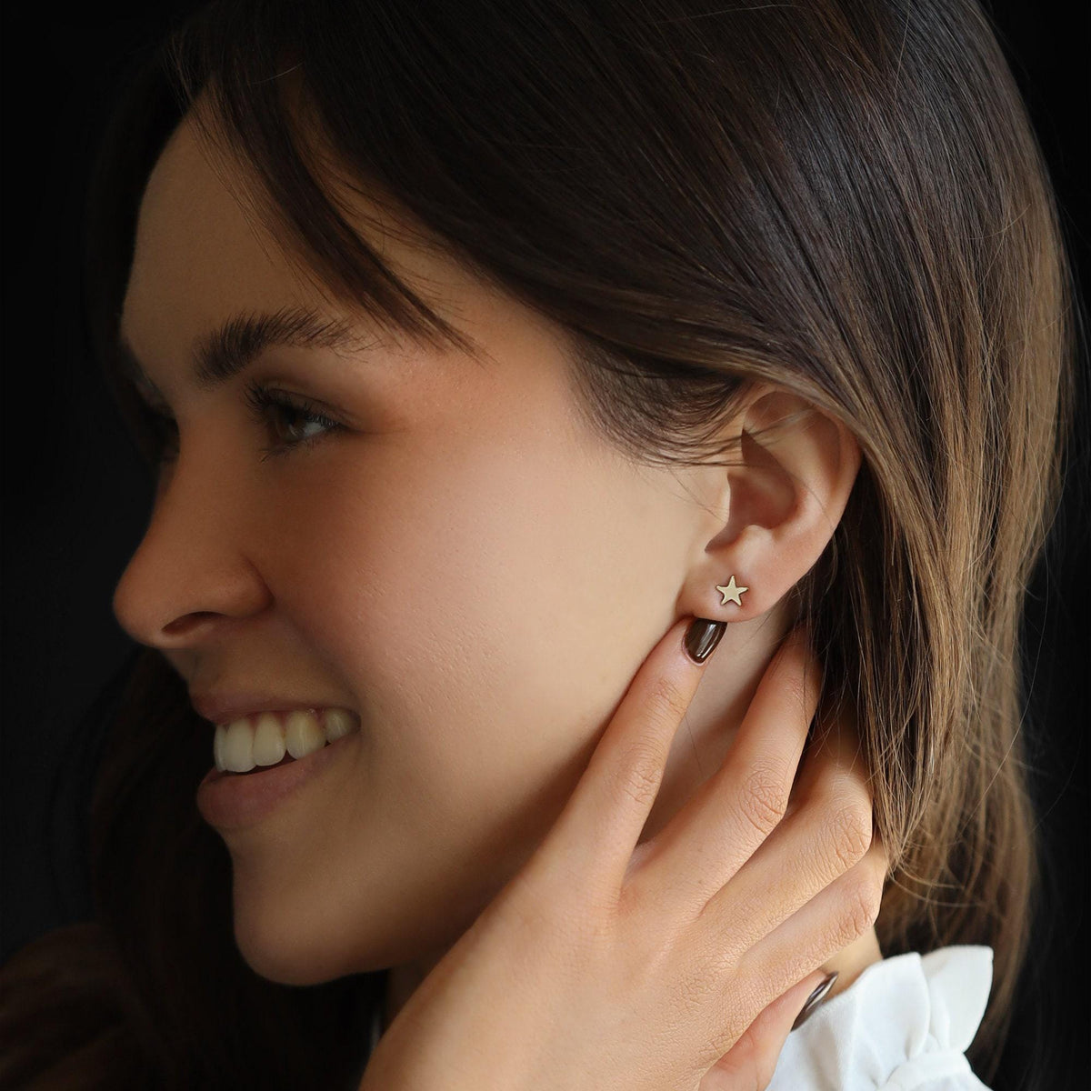 Profile view of a smiling woman wearing a small gold star stud earring in her earlobe.
