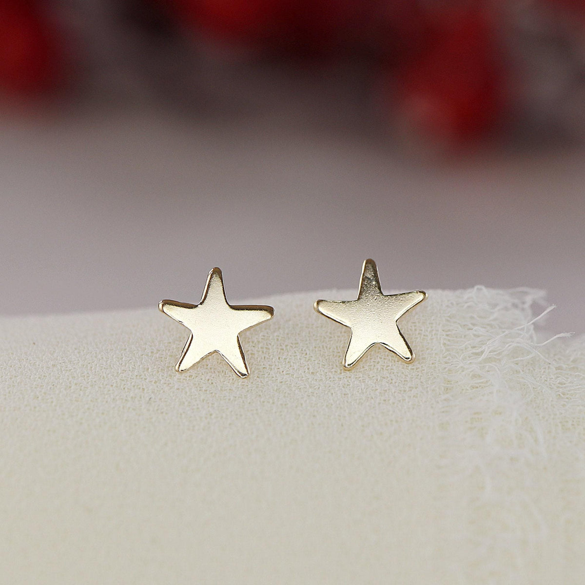 Two polished gold star stud earrings are displayed upright on a light textured cloth.