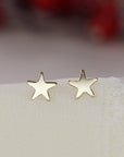 Two polished gold star stud earrings are displayed upright on a light textured cloth.