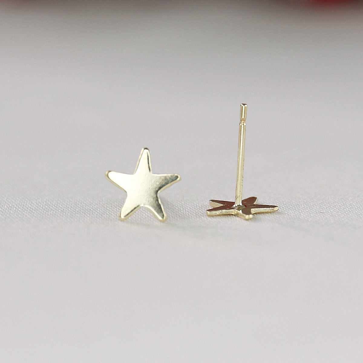 One gold star stud earring stands upright with its post and back fastener visible next to it.