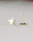One gold star stud earring stands upright with its post and back fastener visible next to it.