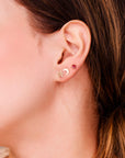 Close-up of an earlobe wearing a gold star stud and crescent moon stud, with a red stone stud higher up.
