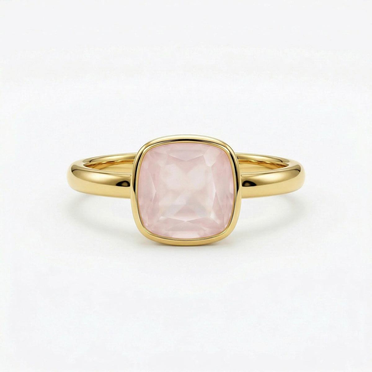 A gold ring featuring a bezel-set, cushion-cut pink gemstone against a plain white background.