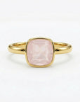 A gold ring featuring a bezel-set, cushion-cut pink gemstone against a plain white background.