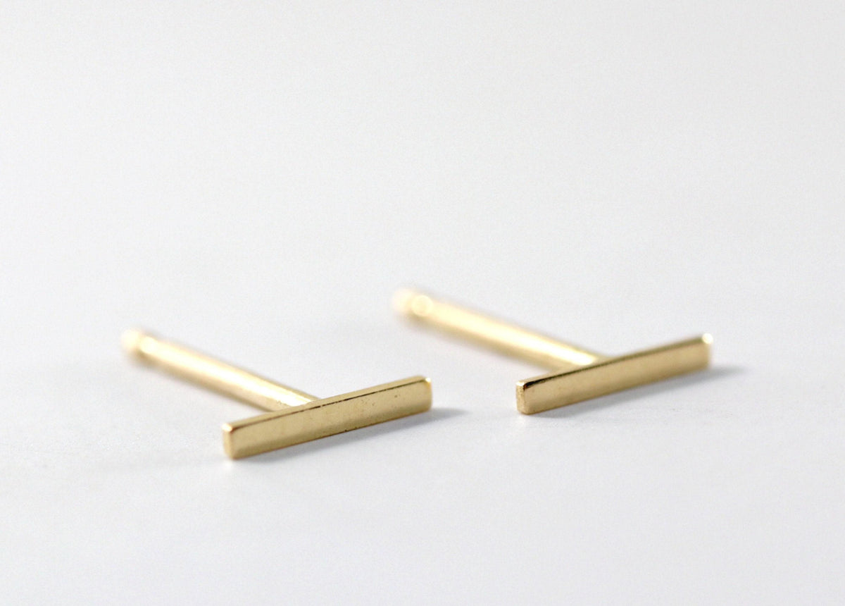 Two gold bar stud earrings shown angled against a plain white background.