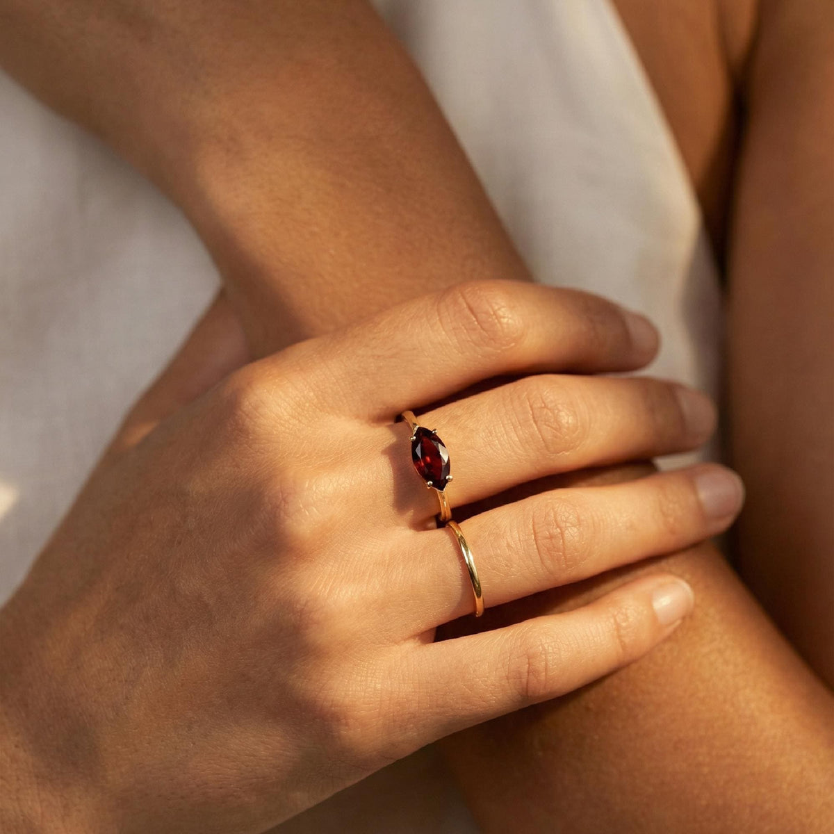 Close-up of hands wearing a gold ring featuring a marquise-cut red garnet stone and a plain gold band.