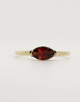 Studio shot of a gold ring centered horizontally with a dark red marquise-cut gemstone against a light background.