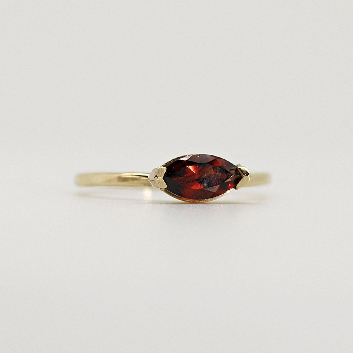 Slightly angled studio view of the thin gold ring holding a horizontally-set marquise red gemstone.