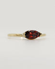 Slightly angled studio view of the thin gold ring holding a horizontally-set marquise red gemstone.