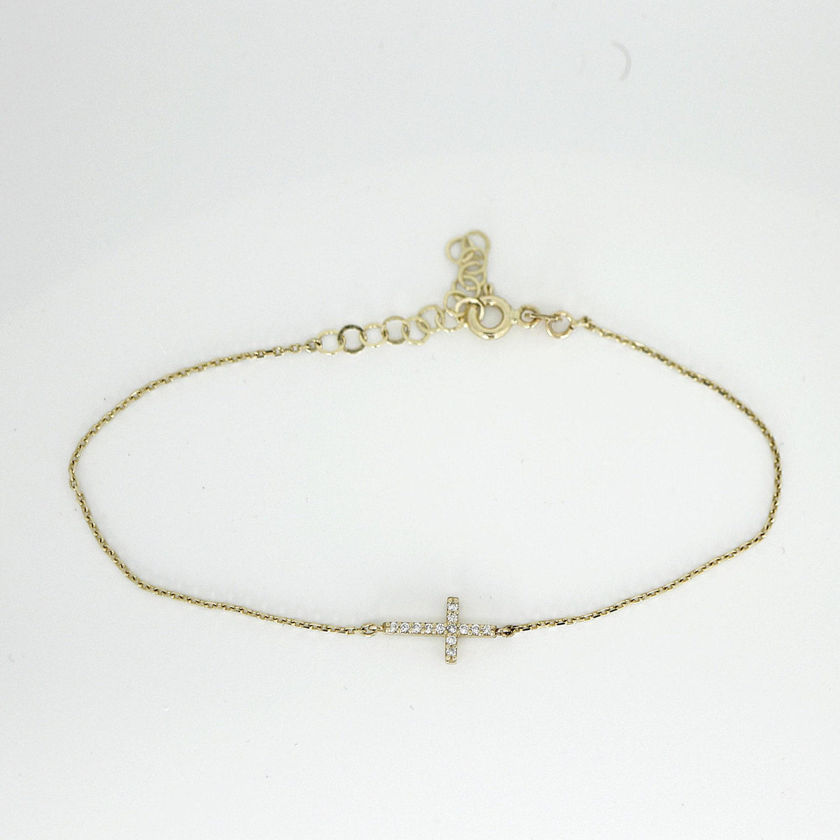 The complete gold bracelet arranged in an oval shape on a plain surface, featuring a diamond cross and an adjustable extension chain.
