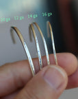 A hand holding four silver cuff bracelets of varying thickness, labeled with green text as 10 ga, 12 ga, 14 ga, and 16 ga.