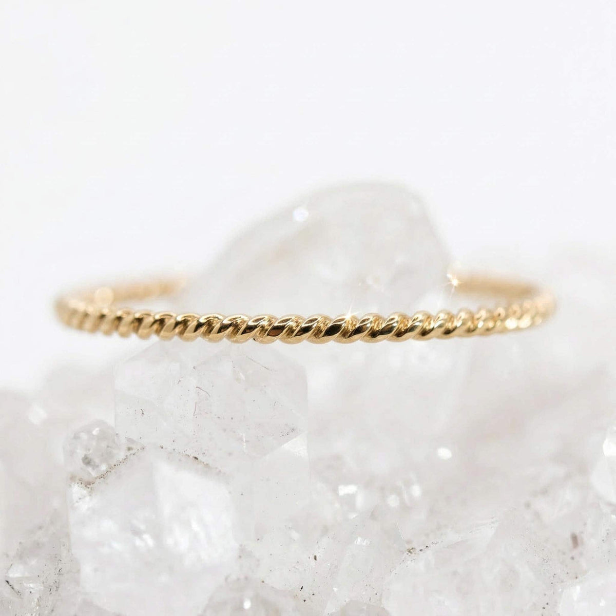 A thin gold twisted rope ring rests horizontally on top of a cluster of white quartz crystals.