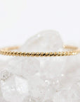 A thin gold twisted rope ring rests horizontally on top of a cluster of white quartz crystals.