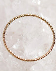 A top-down view of a thin gold twisted rope ring centered on a background of clear and white quartz crystals.