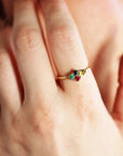 Close-up of a gold ring with multiple colorful gemstones worn on a finger near a person face.