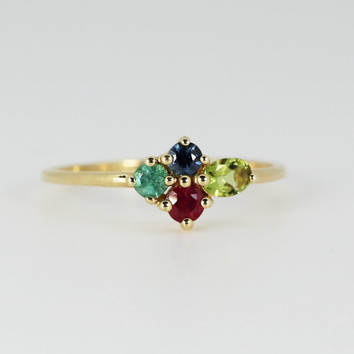 A delicate gold band with a cluster of four multi-colored gemstones displayed on a plain white backdrop.