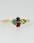 A delicate gold band with a cluster of four multi-colored gemstones displayed on a plain white backdrop.