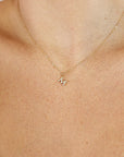 A close-up of a person wearing a dainty gold chain necklace with a small diamond letter M pendant.