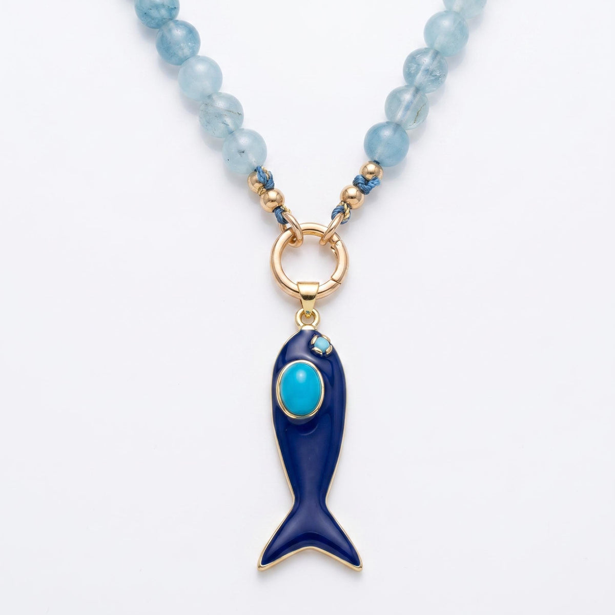 A light blue gemstone beaded necklace hangs against a white background, featuring a round gold clasp holding a dark blue enamel fish pendant with a turquoise stone accent.